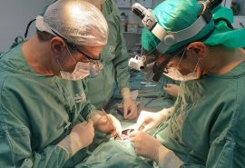 Fotografia. Na imagem, aparecem dois médicos com pijamas de cirurgia de cor verde realizando uma cirurgia cardíaca infantil no coração de um bebê.